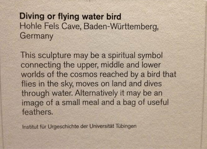 Object label from the British Museum's Ice Age Art exhibition in 2013. The label's title is "Diving or flying water bird" and the text says "This sculpture may be a spiritual symbol connecting the upper, middle and lower worlds of the cosmos reached by a bird that flies in the sky, moves on land and dives through water. Alternatively it may be an image of a small meal and a bag of useful feathers."
